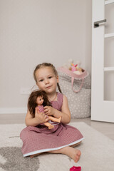 Cute little girl playing with a doll whille sitting on the carpet in her room