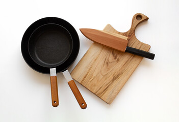 New frying pan set, wooden cutting board and kitchen knife isolated on white background. Top view.
