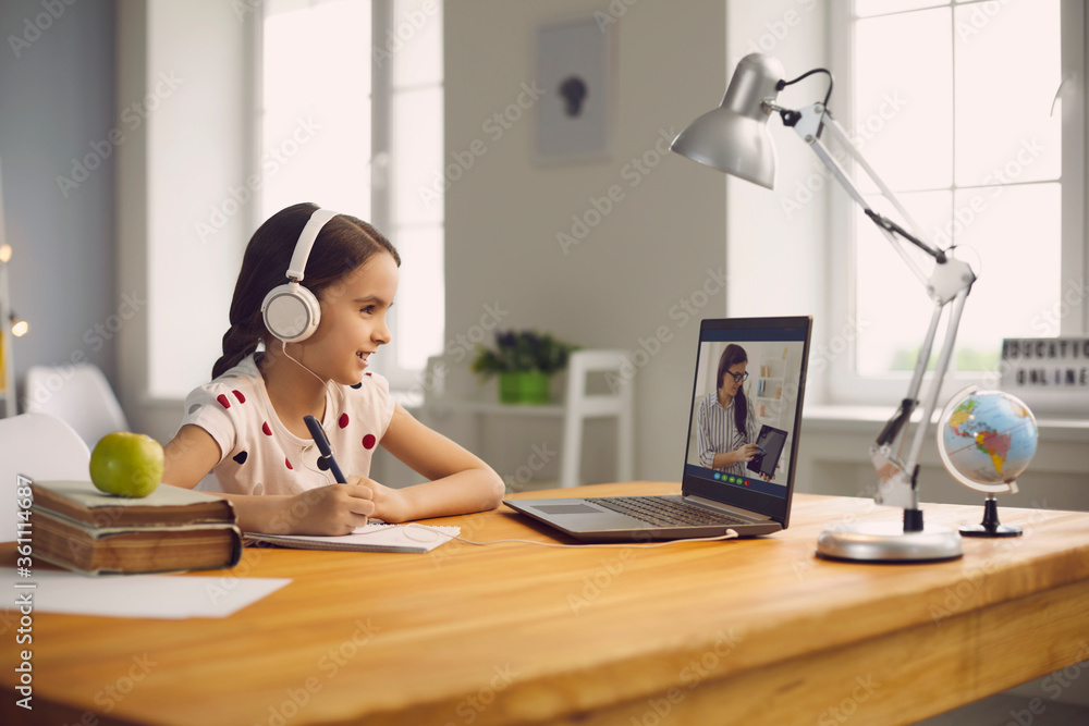 Online student education. Schoolgirl listens to a lecture of a teacher using a laptop video call lesson sitting at a table at home. - obrazy, fototapety, plakaty 