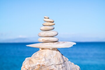 Canvas Print - Closeup shot of pebbles stacked on each other in a balance with the blue sea in the background