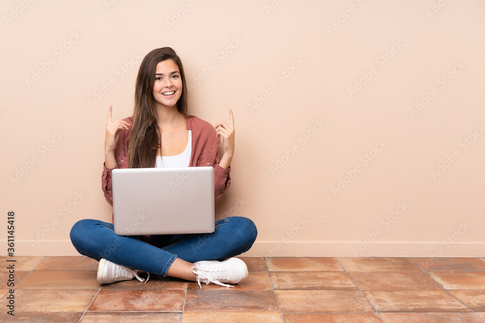 Teenager student girl sitting on the floor with a laptop pointing up a great idea - obrazy, fototapety, plakaty 