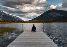 Man Backpacker Sitting On Wooden Pier In Vermillion Lake At Banff National Park