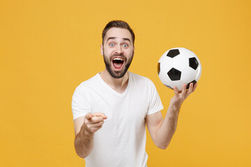 Shocked bearded man guy football fan in white t-shirt isolated on yellow background. People sport family leisure concept. Cheer up support favorite team with soccer ball point index finger on camera.