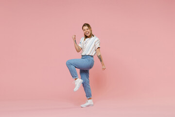 Joyful young blonde woman girl in casual striped shirt posing isolated on pastel pink background studio portrait. People sincere emotions lifestyle concept. Mock up copy space. Doing winner gesture.