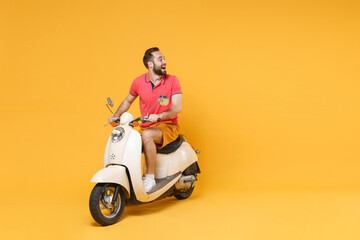 Wall Mural - Cheerful young bearded man guy in casual summer clothes driving moped isolated on yellow wall background studio portrait. Driving motorbike transportation concept. Mock up copy space. Looking aside.