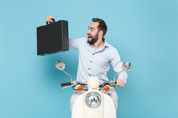 Wall Mural - Cheerful young bearded man guy in casual light shirt driving moped isolated on pastel blue wall background studio portrait. Driving motorbike transportation concept. Mock up copy space Hold briefcase.