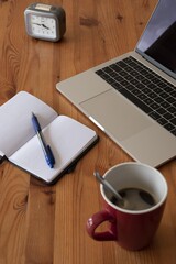 Canvas Print - Vertical shot of a laptop, clock, notebook with a pen and a cup of coffee on a wooden table