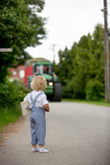 Wall Mural - Blond toddler boy in vingate clothes holding book, standing on the street waiting for a bus