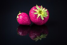 Horizontal Shot Of Two Purple Strawberries With A Reflection On A Black Surface