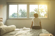 © Creativa Images - Young woman sits on bed while enjoys sunset view