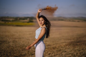 Poster - Horizontal shot of a female posing with a smoke bomb on a background of fields and windmills