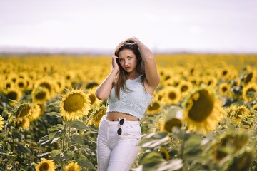 Poster - Horizontal shot of a caucasian young female posing in a bright field of sunflowers on a sunny day