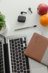 Sticker - Vertical shot of a notebook planner on a laptop with fruits, pen and wireless earphones