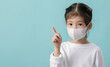 © DN6 - Asian little child girl wearing respirator mask to protect coronavirus outbreak and pointing hand to blank background, New virus Covid-19 from Wuhan China concept, Empty space on blue long banner