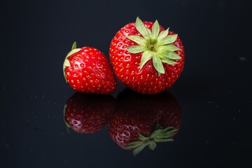 Horizontal shot of two red Croatian strawberries on a black reflecting surface