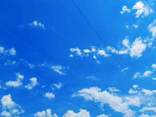 Black electrical wires stretched diagonally across the entire image against a clear cloudy sky on a bright sunny day. The combination of nature and industry.