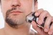 © aaalll3110 - isolated on a white background: a man shaves his stubble. the guy cleans his beard with an electric razor. morning treatments in the bathroom. half of the beard close-up. copy space