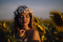 Young Brunette Female In A Flower Crown With Closed Eyes Enjoying The Sun In A Sunflower Field