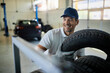Happy repairman stacking car tires in auto repair shop.
