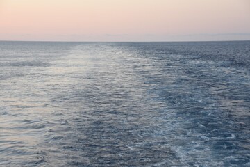 Vessel`s keel water during calm weather and sunset Ship is tranquil sailing through the blue ocean in the background is sky with orange and red color