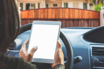 Woman in car hand holding and using modern white digital tablet computer pc with blank screen on modern home blurred background. Home security and online camera viewed concept. 