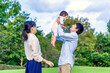 © chikala - 緑の樹木を背景に赤ちゃんを抱き上げ遊ぶ夫婦