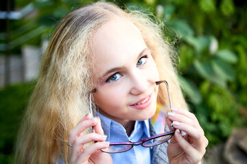 Wall Mural - Pretty teenage girl 14-16 year old with curly long blonde hair and in glasses in the green park in a summer day outdoors. Beautiful portrait