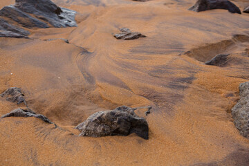 natural filled frame close up wallpaper background early morning photo of sharp brown black rocks on a wet yellow orange sand beach. Sri Lanka