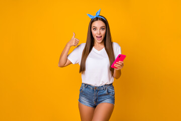 Astonished surprised girl promoter use smartphone show thumb up sign recommend incredible ads promotion impressed wear white blue headband denim jeans isolated bright shine color background