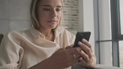 Wall Mural - Carefree attractive blonde woman using smartphone while sitting on sofa at home