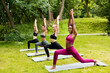 Diverse young women making warrior pose during their outdoor yoga practice at park, blank space