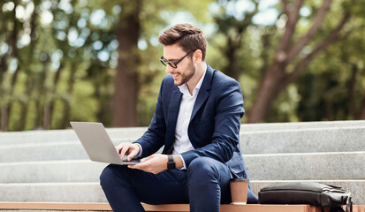 Happy entrepreneur working with laptop computer while sitting on stairs in urban park