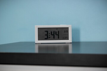 Poster - Closeup of a white digital clock on a table against a blue wall