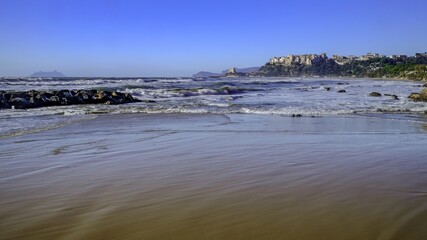 Sticker - Panoramic view of a wavy ocean shore with urban settling on the background