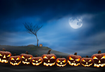 Lots of halloween lanterns with evil face and eyes, Jack O Lantern, against a spooky looking landscape background at night with a glowing full moon, lone tree and cloudy sky.