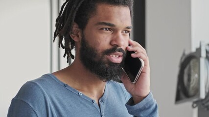 Wall Mural - A calm relaxed young african american man is talking on the smartphone in the living room at home