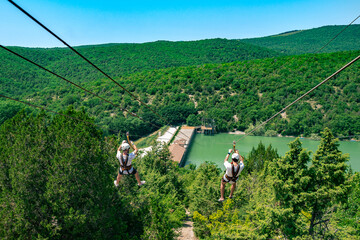 Two guys down a cable in a green valley. Rope descent with a carbine against the backdrop of a huge forest.