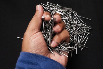 Sticker - Closeup shot of a male hand holding steel nails on black background