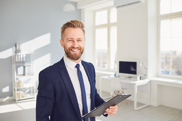 Wall Mural - Positive businessman worker manager holds a clipboard in his hand smiling works in modern office.