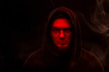 A Warlock With A Red Face In A Hood And Glasses On A Black Background In Smoke.