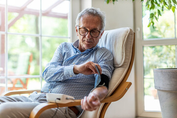 Wall Mural - Senior man using medical device to measure blood pressure
