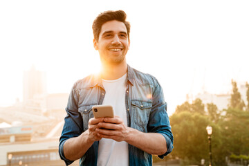 Poster - Photo of joyful handsome man smiling and using mobile phone