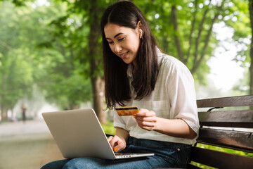 Poster - Photo of happy asian woman using laptop and holding credit card