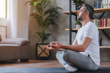 Meditation Concept. Calm Man Meditating While Sitting In Lotus Position Relaxing Doing Yoga At Home
