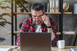 © InsideCreativeHouse - Thoughtful businessman in eyewear looking at computer screen, sitting at table at home