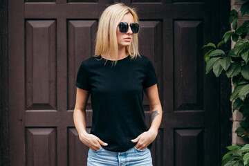 Wall Mural - Stylish blonde girl wearing black t-shirt and glasses posing against street , urban clothing style. Street photography