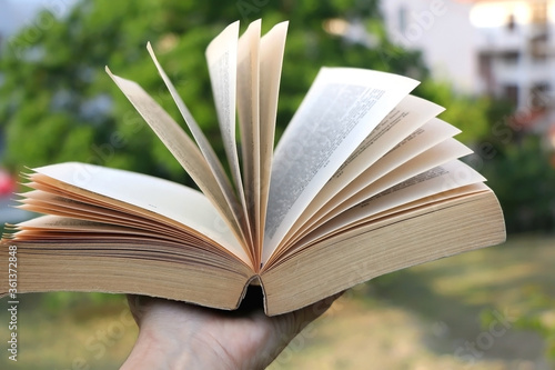 Obraz Dibond Hand holding open book in a garden. Selective focus.