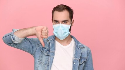 Sticker - Sad young man guy 20s in denim jacket white t-shirt sterile face mask showing thumbs down isolated on pastel pink background studio. Epidemic pandemic coronavirus 2019-ncov sars covid-19 virus concept