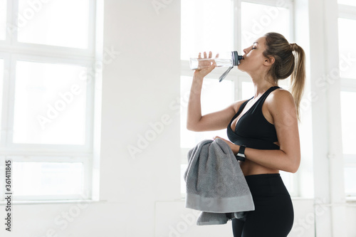 Tired sweaty woman drinks water after fitness workout in the gym