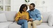 © VAKSMANV - Happy African American couple husband and wife sitting on sofa using tablet and credit card for online shopping at home.